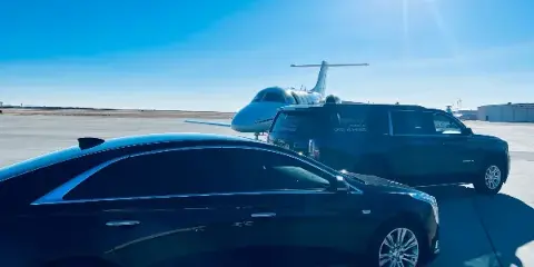 A black sedan and a black SUV with 'Elegance' branding parked on an airport tarmac in front of a private jet.