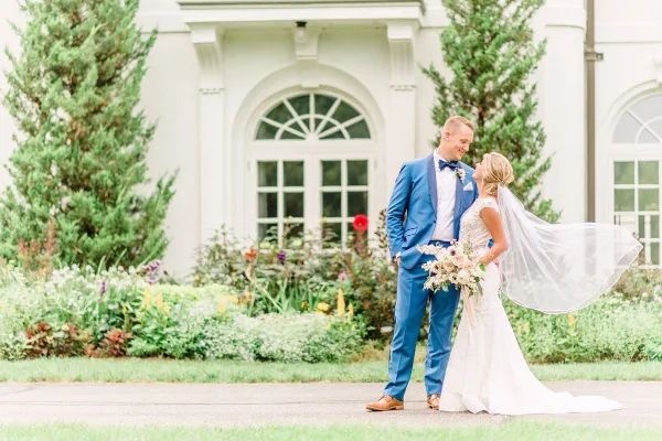 Bride and groom standing together in front of a white venue building with gardens.