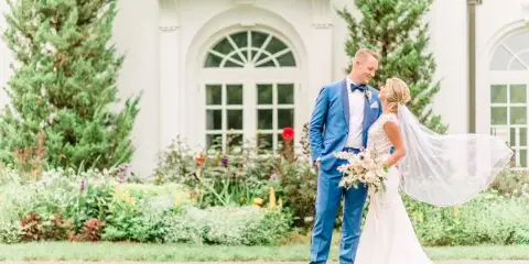 Bride and groom standing together in front of a white venue building with gardens.