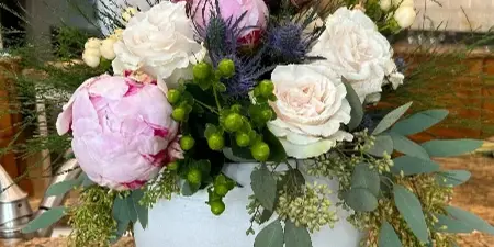 A lush floral arrangement with pink peonies, white roses, and greenery in a white vase on a kitchen counter.
