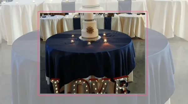 A wedding cake table decorated with a navy blue tablecloth, candles, and illuminated LOVE letters.