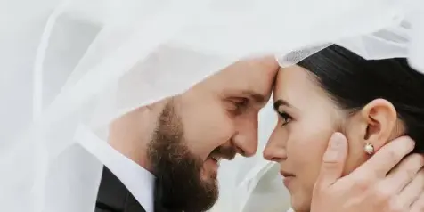 A bride and groom looking at each other under a veil, with the bride's hair and makeup visible.