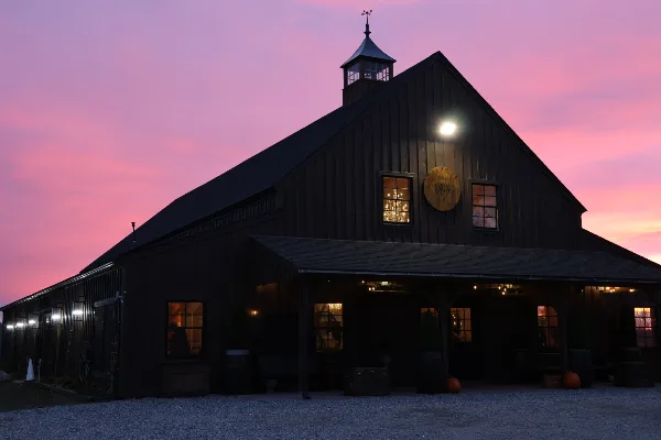 Exterior view of the SaltWater Fields event barn at dusk, featuring a dark wooden facade, a cupola, and a circular logo on the wall.