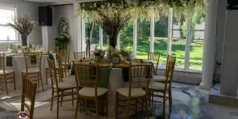 Indoor wedding reception venue with decorated tables, gold chairs, and floral arrangements.