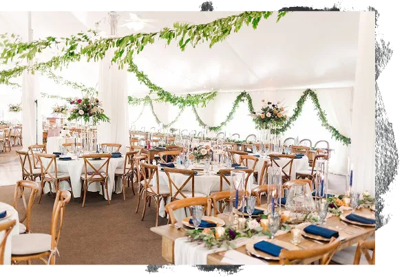 A wedding reception hall decorated with floral centerpieces, greenery garlands, and set dining tables.