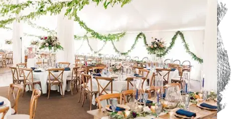 A wedding reception hall decorated with floral centerpieces, greenery garlands, and set dining tables.