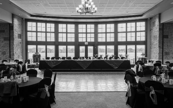 Interior view of a large event ballroom with round tables, a head table, and floor-to-ceiling windows looking out onto a lake.