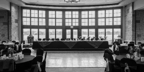 Interior view of a large event ballroom with round tables, a head table, and floor-to-ceiling windows looking out onto a lake.