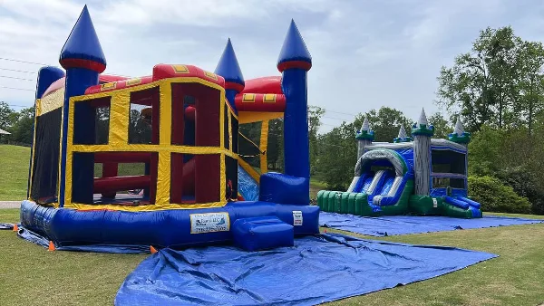 A large blue and yellow inflatable castle bounce house and a water slide set up on a lawn, featuring a banner for Clay County Party Rental LLC.