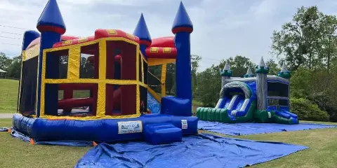 A large blue and yellow inflatable castle bounce house and a water slide set up on a lawn, featuring a banner for Clay County Party Rental LLC.