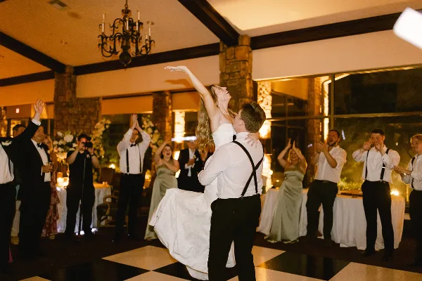 A bride and groom dancing at a wedding reception while guests applaud and celebrate in a banquet hall.