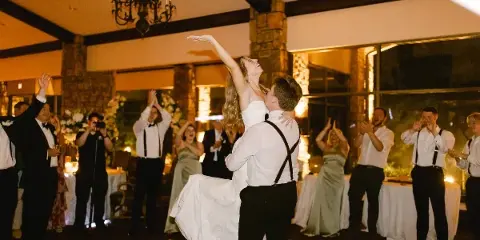 A bride and groom dancing at a wedding reception while guests applaud and celebrate in a banquet hall.
