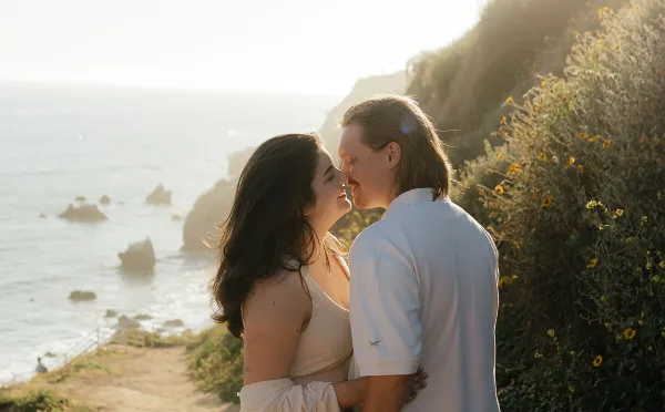A couple sharing an intimate moment outdoors near a coastline during golden hour.