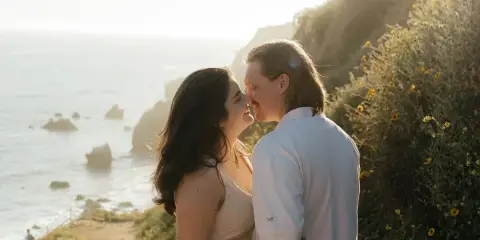 A couple sharing an intimate moment outdoors near a coastline during golden hour.
