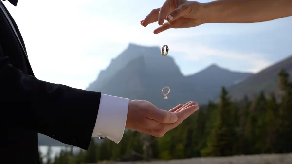 A close-up of hands exchanging wedding rings with a mountain landscape in the background.