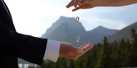 A close-up of hands exchanging wedding rings with a mountain landscape in the background.