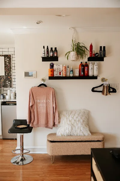 Interior view of a salon suite featuring a pink sweatshirt with 'The Salon Suites' logo, shelves of hair products, and a salon chair.