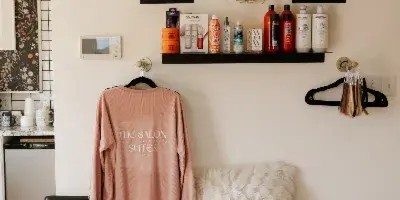 Interior view of a salon suite featuring a pink sweatshirt with 'The Salon Suites' logo, shelves of hair products, and a salon chair.
