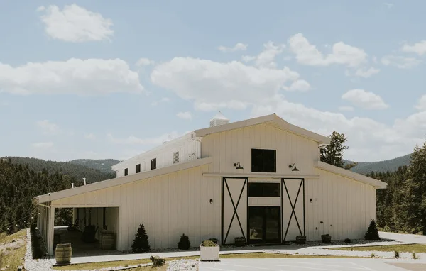 Exterior view of a white barn-style wedding venue building with a covered patio and mountain views.