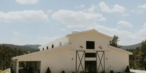 Exterior view of a white barn-style wedding venue building with a covered patio and mountain views.