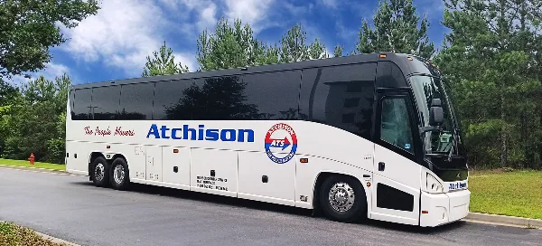 A white and black Atchison Transportation motorcoach parked on a paved road with trees in the background.