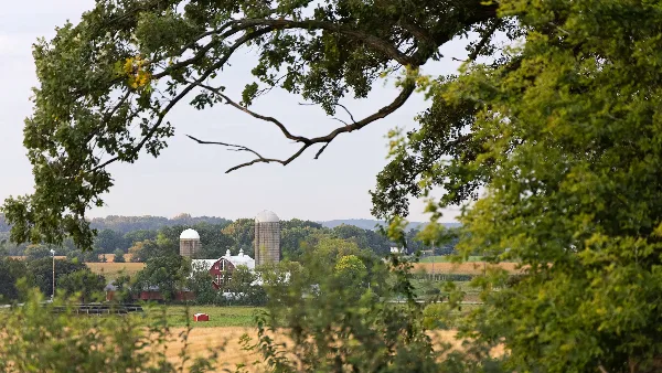 A view of a farm with a red barn and silos framed by trees and fields.