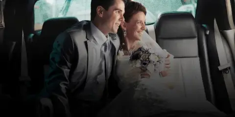A smiling bride and groom sitting together in the back seat of a car.
