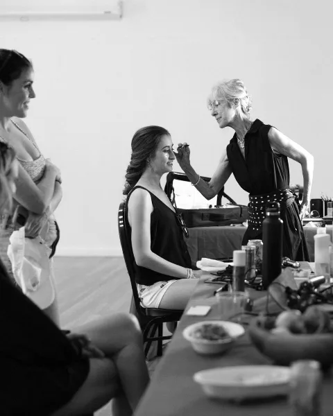 A makeup artist applying makeup to a seated client in a studio environment.