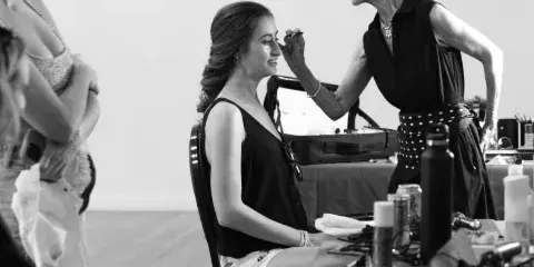 A makeup artist applying makeup to a seated client in a studio environment.