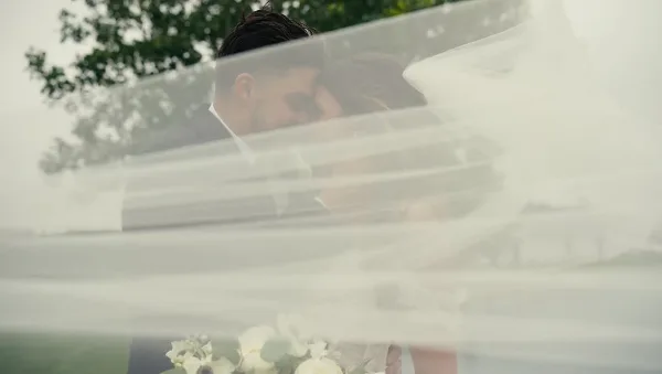A bride and groom embracing behind a flowing white veil.