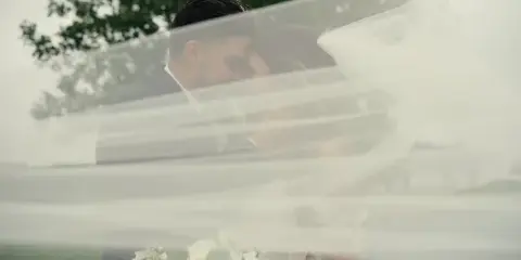 A bride and groom embracing behind a flowing white veil.