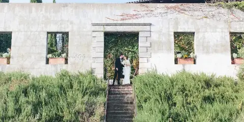 Bride and groom kissing on stone steps in front of a concrete building with greenery