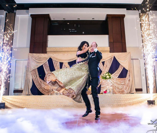 A couple dancing at a wedding reception with cold sparklers and a decorated stage backdrop.