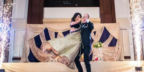 A couple dancing at a wedding reception with cold sparklers and a decorated stage backdrop.