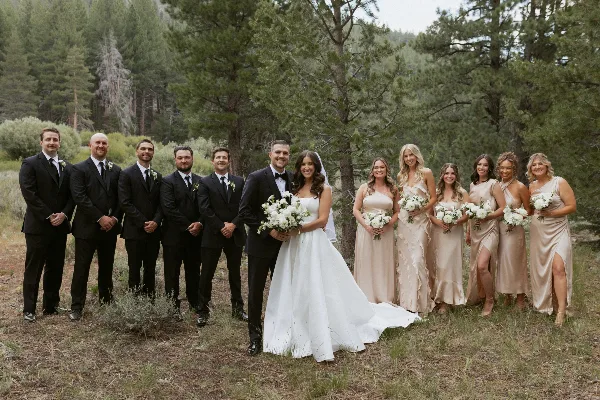 A wedding party consisting of a bride, groom, and attendants posing outdoors in a forest setting.