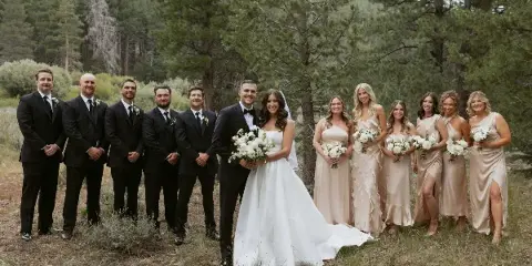 A wedding party consisting of a bride, groom, and attendants posing outdoors in a forest setting.