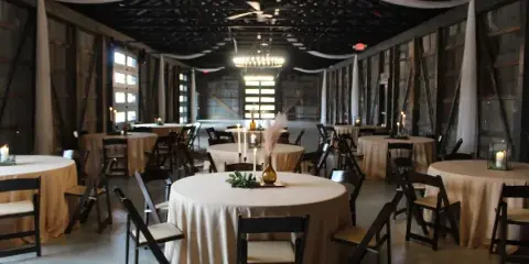 Interior view of a rustic event venue with round tables, chairs, and chandeliers.