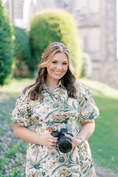 Portrait of a smiling woman holding a professional camera outdoors