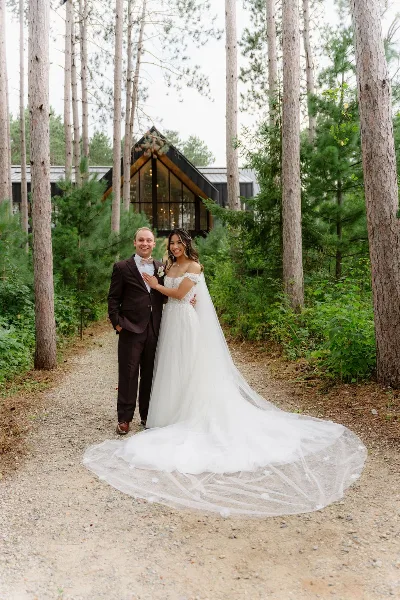 A bride and groom standing together on a forest path in wedding attire.