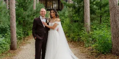 A bride and groom standing together on a forest path in wedding attire.