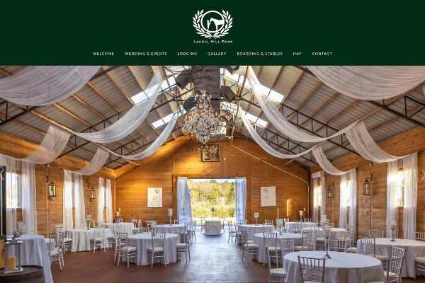Interior view of a wooden barn-style wedding venue with round tables, white drapery, and a chandelier.