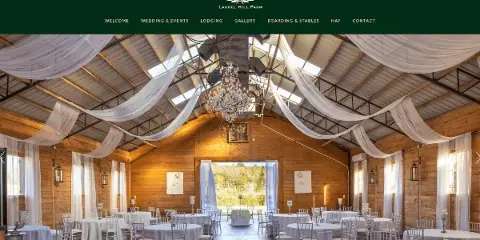 Interior view of a wooden barn-style wedding venue with round tables, white drapery, and a chandelier.