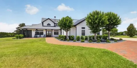 Exterior view of a white and dark-trimmed venue building with a brick driveway and manicured lawn.