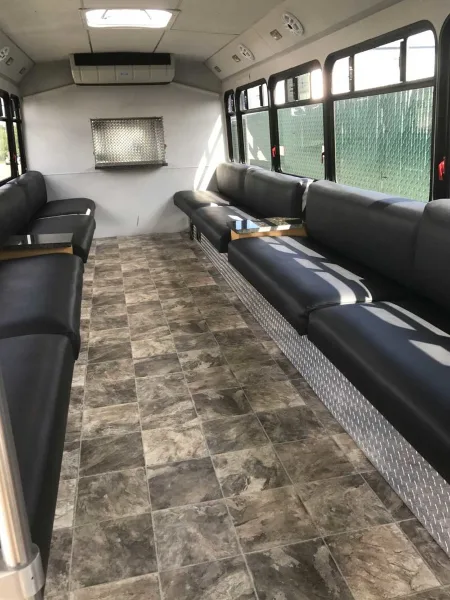 Interior view of a party bus showing black leather bench seating and tiled flooring.