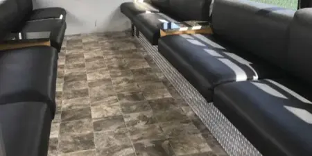 Interior view of a party bus showing black leather bench seating and tiled flooring.