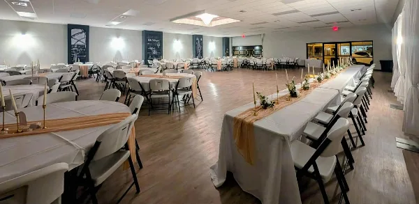 Interior view of a large event venue with round tables and a long head table set for a wedding reception.