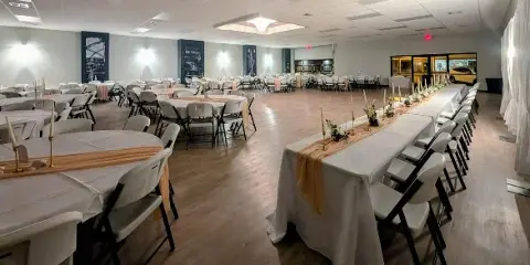 Interior view of a large event venue with round tables and a long head table set for a wedding reception.