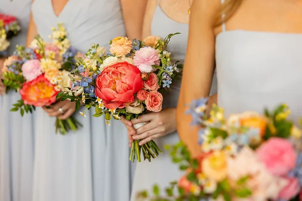 Bridesmaids in light blue dresses holding garden-style wedding bouquets with peonies and roses