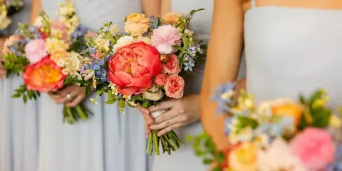 Bridesmaids in light blue dresses holding garden-style wedding bouquets with peonies and roses