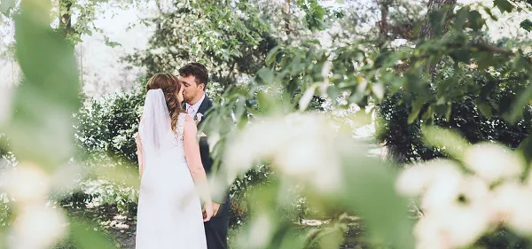 A bride and groom sharing a kiss in an outdoor garden setting.
